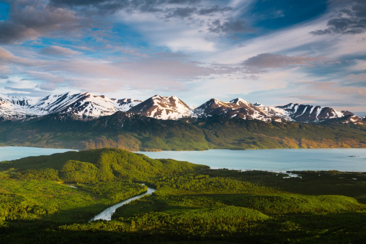 Blue waters separate large snow covered mountains from mossy green lands 