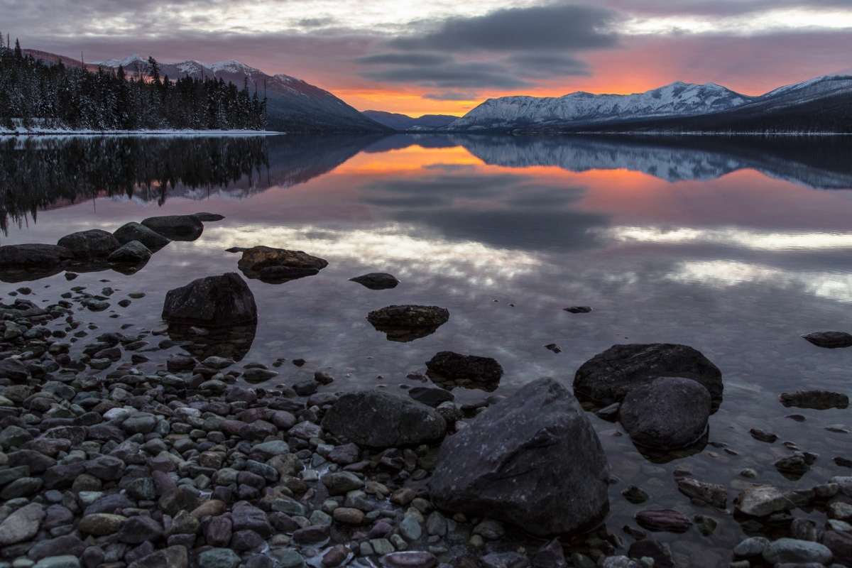 Shot from the ground, this photo showcases the beautifully colored rocks and a sunset over mountain tops and the lake. 