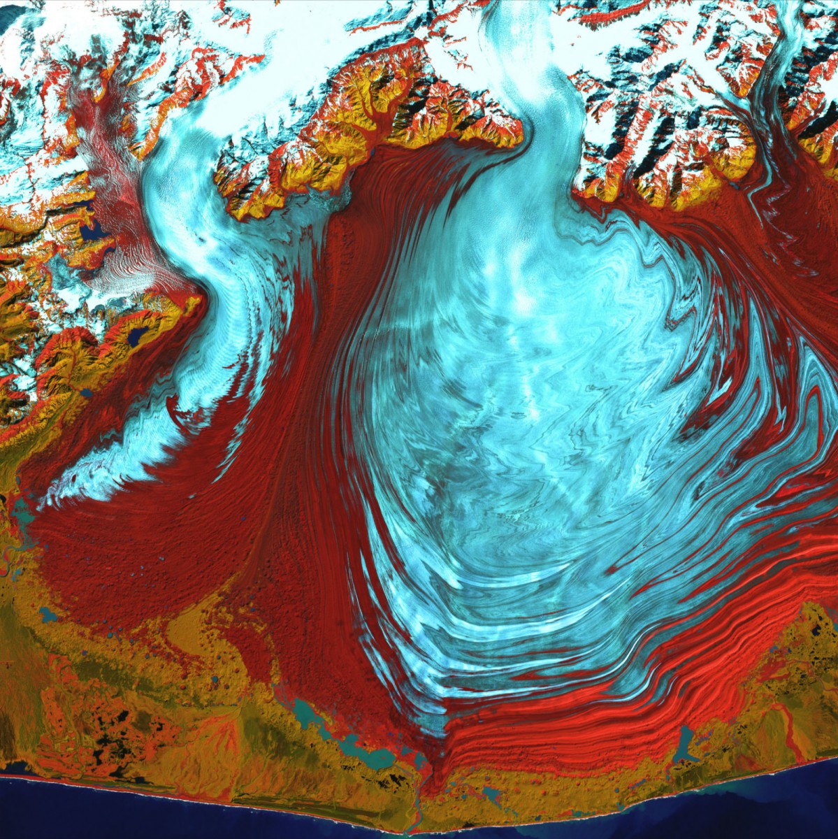 A colorful satellite photo showing a glacier as a light blue puddle spreading out across a red and orange rippled plain.