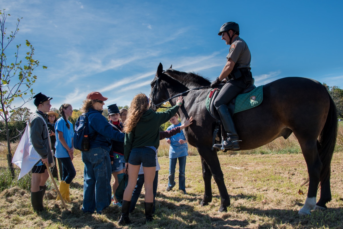 Children gather around to pet a horse ridden by a Park Ranger 