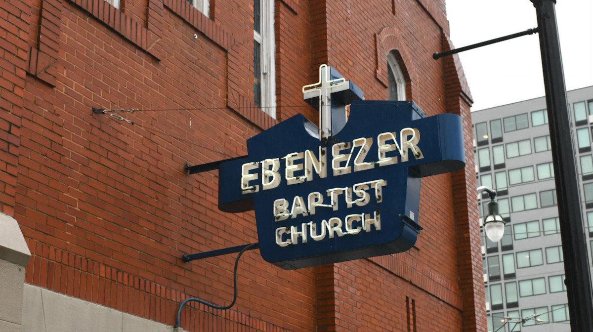 A blue metal sign reading "Ebenezer Baptist Church" is attached to the brick wall of a church.