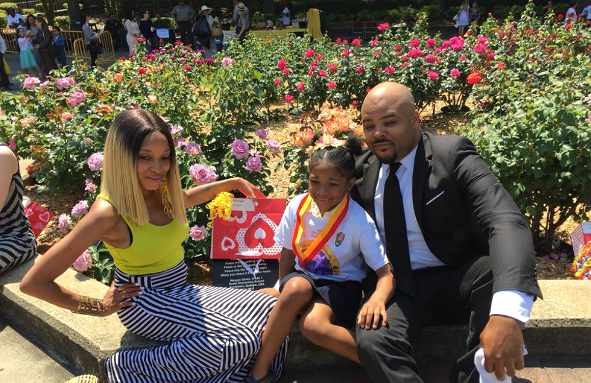 An African American man, woman and little girl pose in front of a large rose garden.