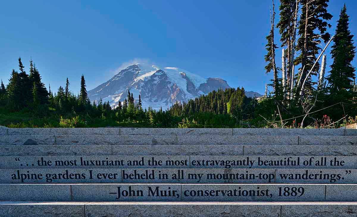 Stone steps are engraved with conservationist John Muir's quote, "...the most luxuriant and the most extravagantly beautiful of all the alpine gardens I ever beheld in my mountain-top wanderings." Far behind the steps is the silhouette of a snowy mountain.