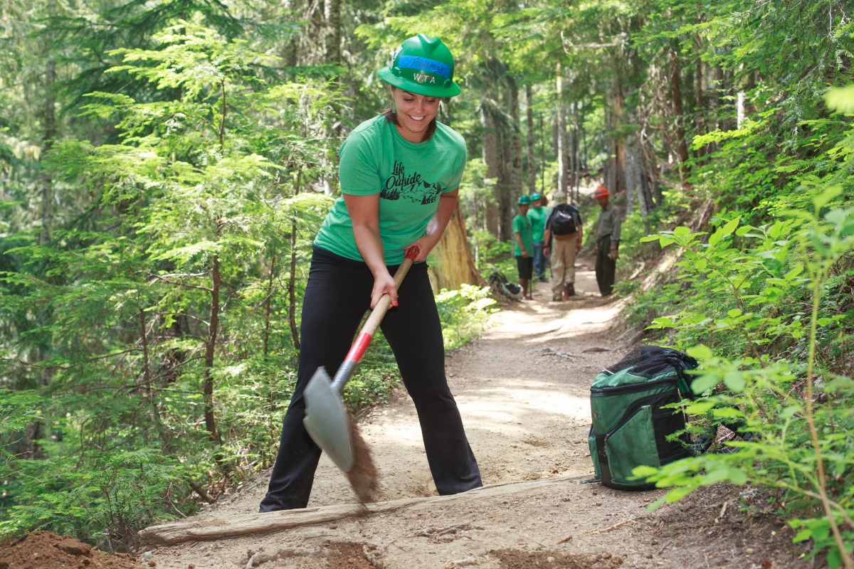 A volunteer uses a shovel to help maintain the trail.