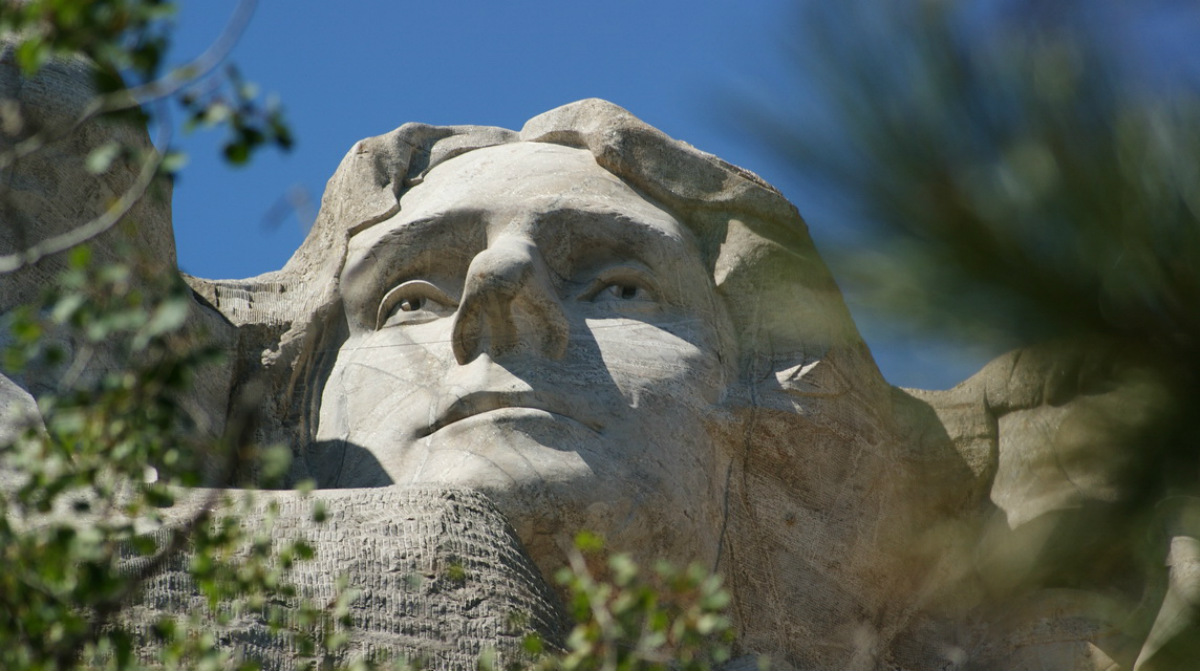 The stone face of Thomas Jefferson carved into the side of Mount Rushmore looks out.