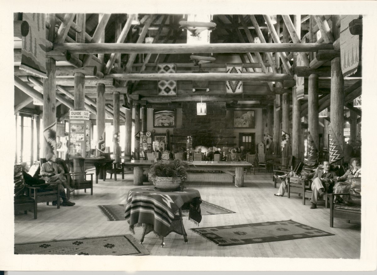 The interior of an historic hotel is lavishly constructed with wooden rafters and rustic chandeliers and decorated with patterned rugs and comfortable armchairs.