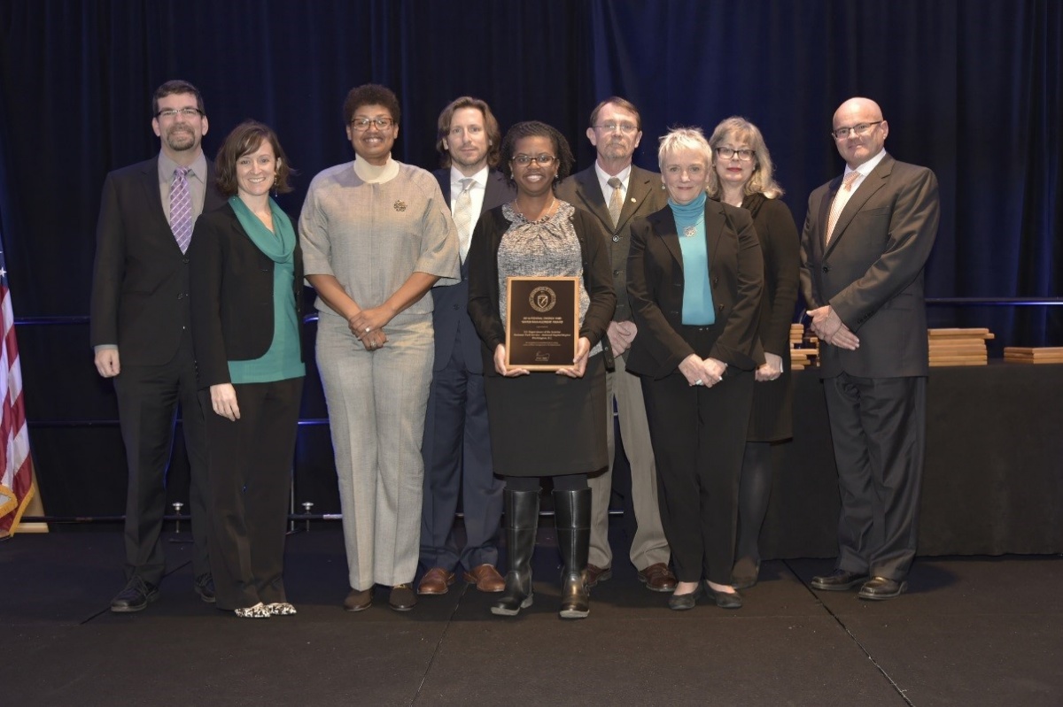 A small group of men and women pose while holding an award plaque.