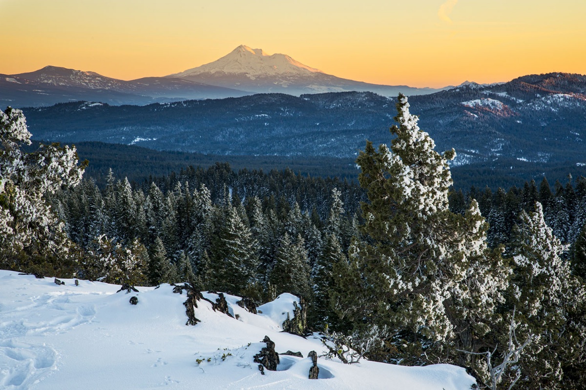 Snow covers a gorgeous valley landscape with mountains rising in the background.