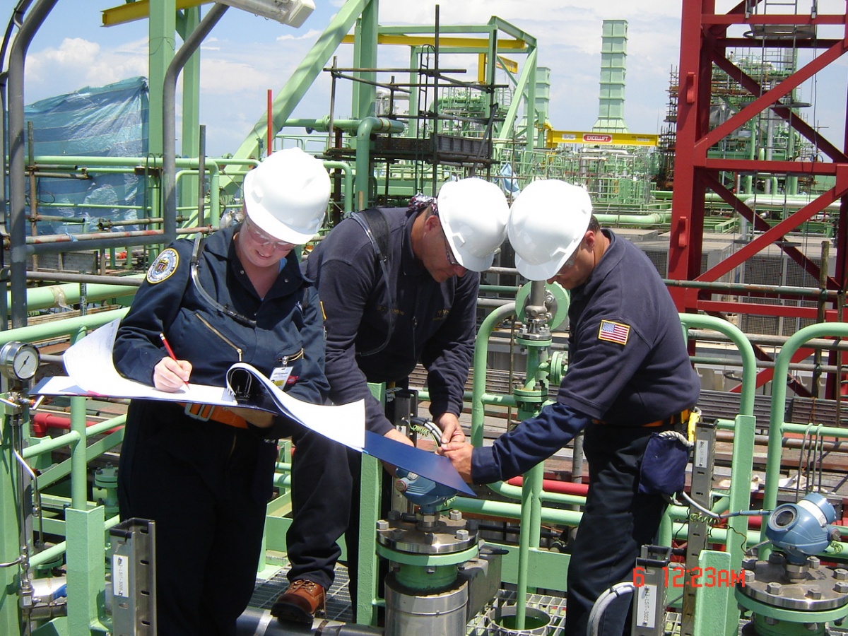 Three people in hardhats inspect machinery on an oil rig.