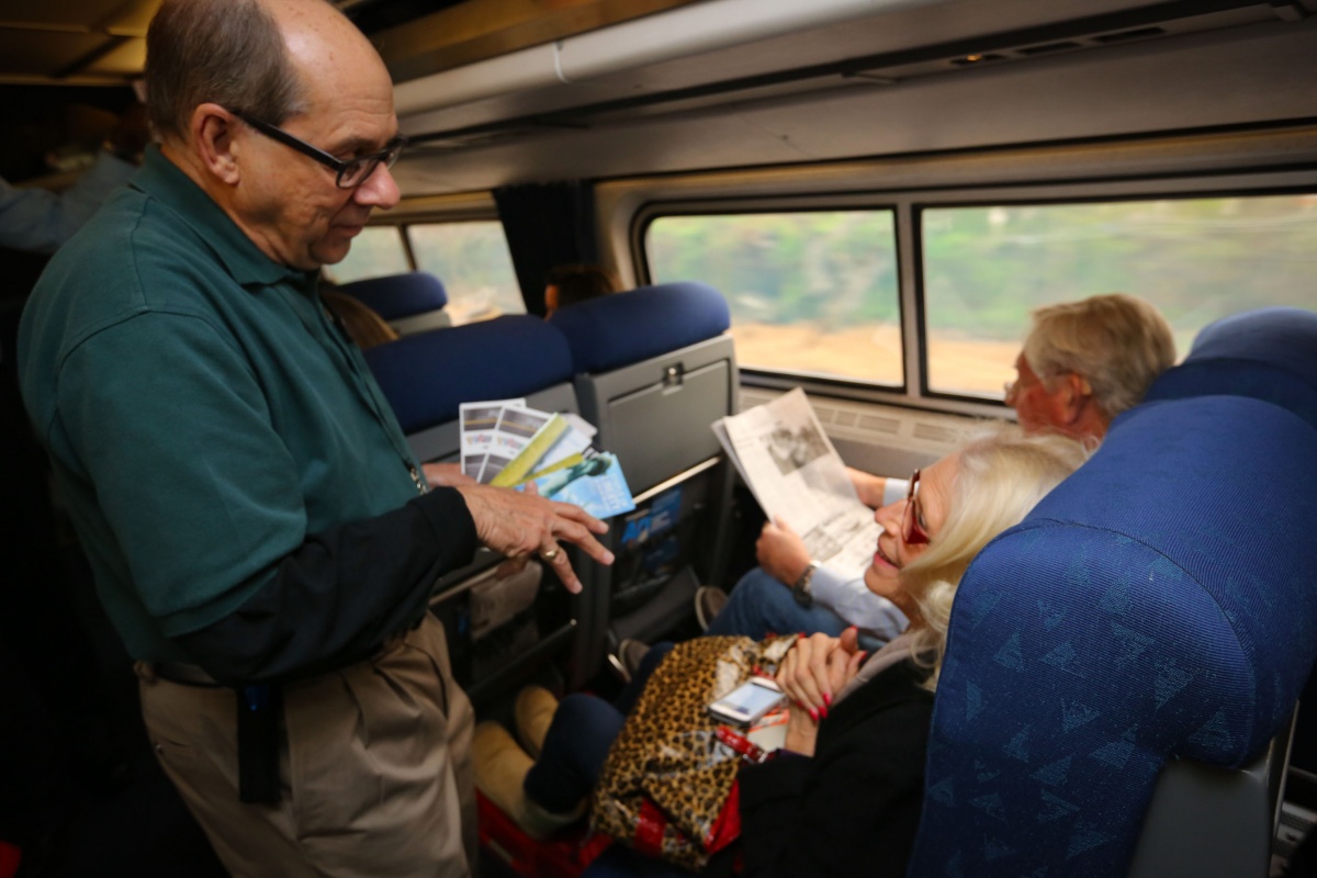 A volunteer wearing a green shirt passes out pamphlets to two seated passengers.