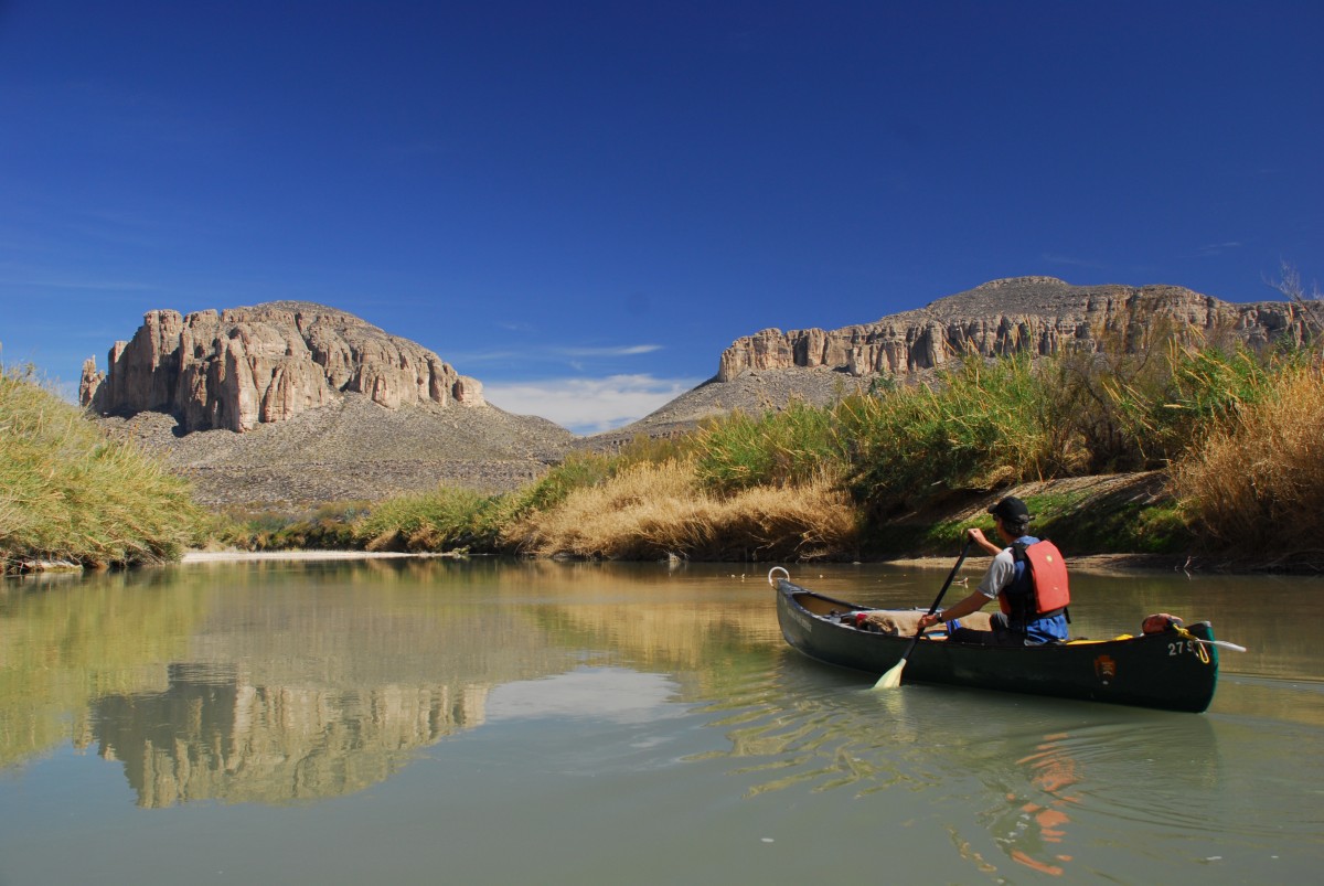 Man in red life jacket paddles blue canoe through Rio Grande Wild and Scenic River.
