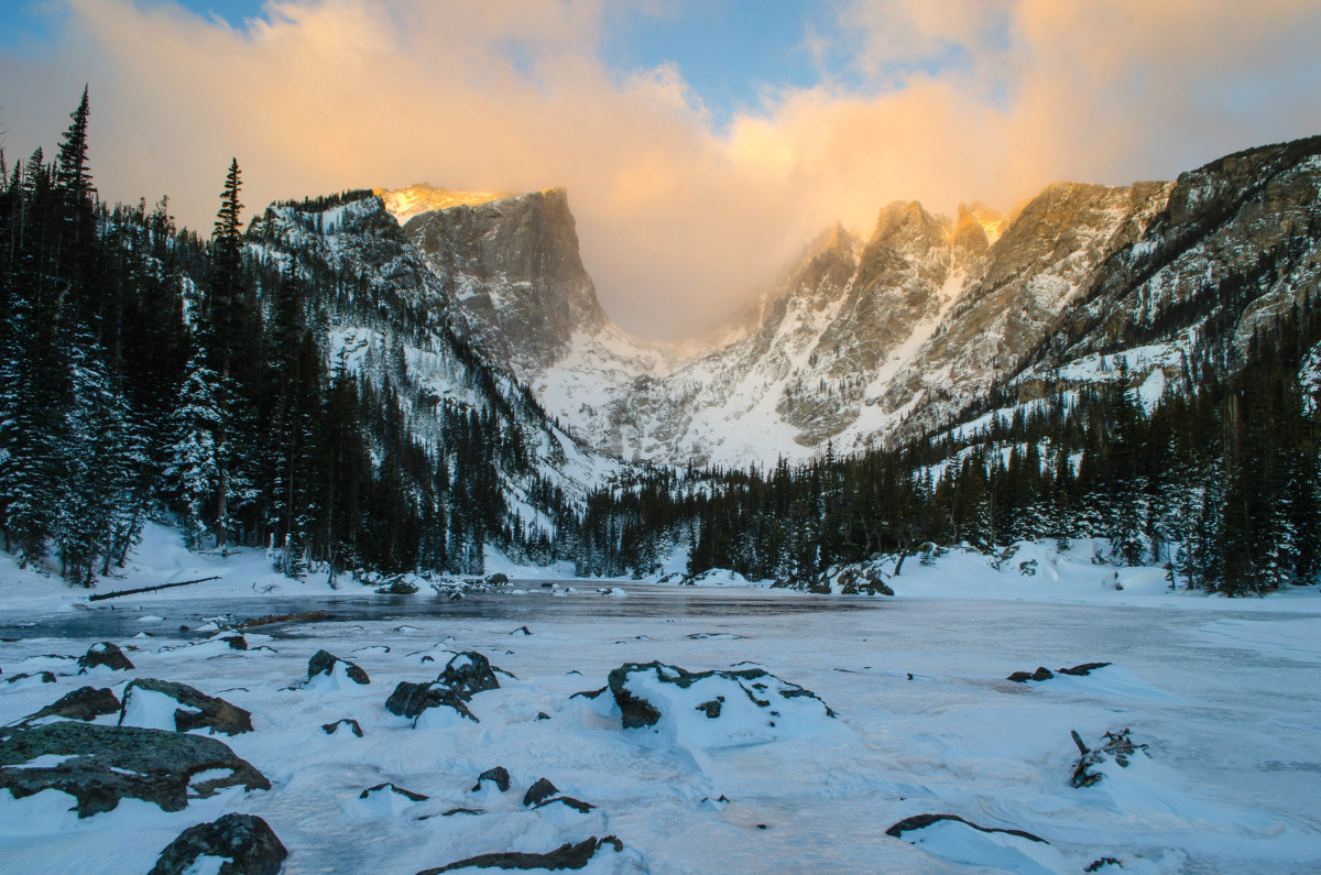 A frozen lake is surrounded by tall rocky mountains on a cloudy day.