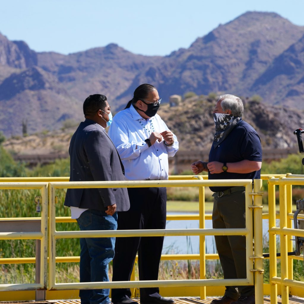 Secretary Bernhardt wears a mask and stands on a metal walkway over a wetland talking with two other men wearing masks.