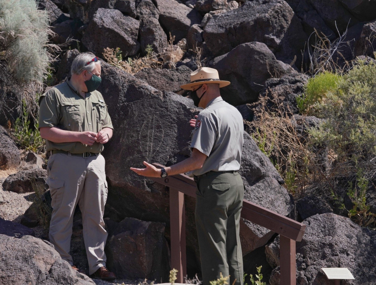 Secretary Bernhardt stands on a hiking trail next to some boulders and talks with a white male park ranger.