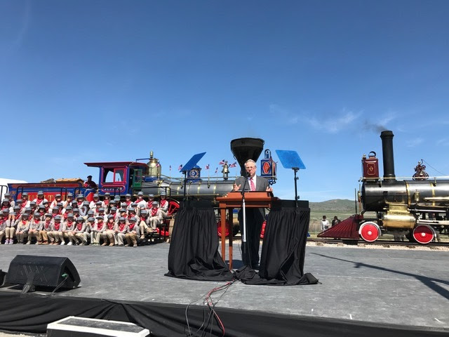 Secretary Bernhardt speaking on a podium with decorated classic trains as a backdrop.