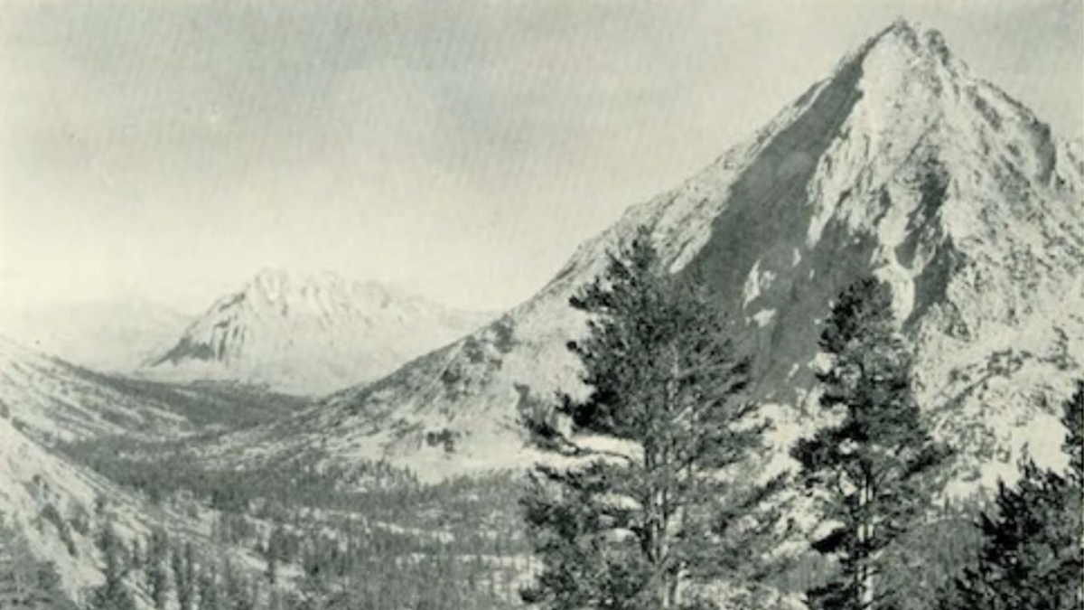 An old black and white photo of a cone shaped mountain rising above a forest.