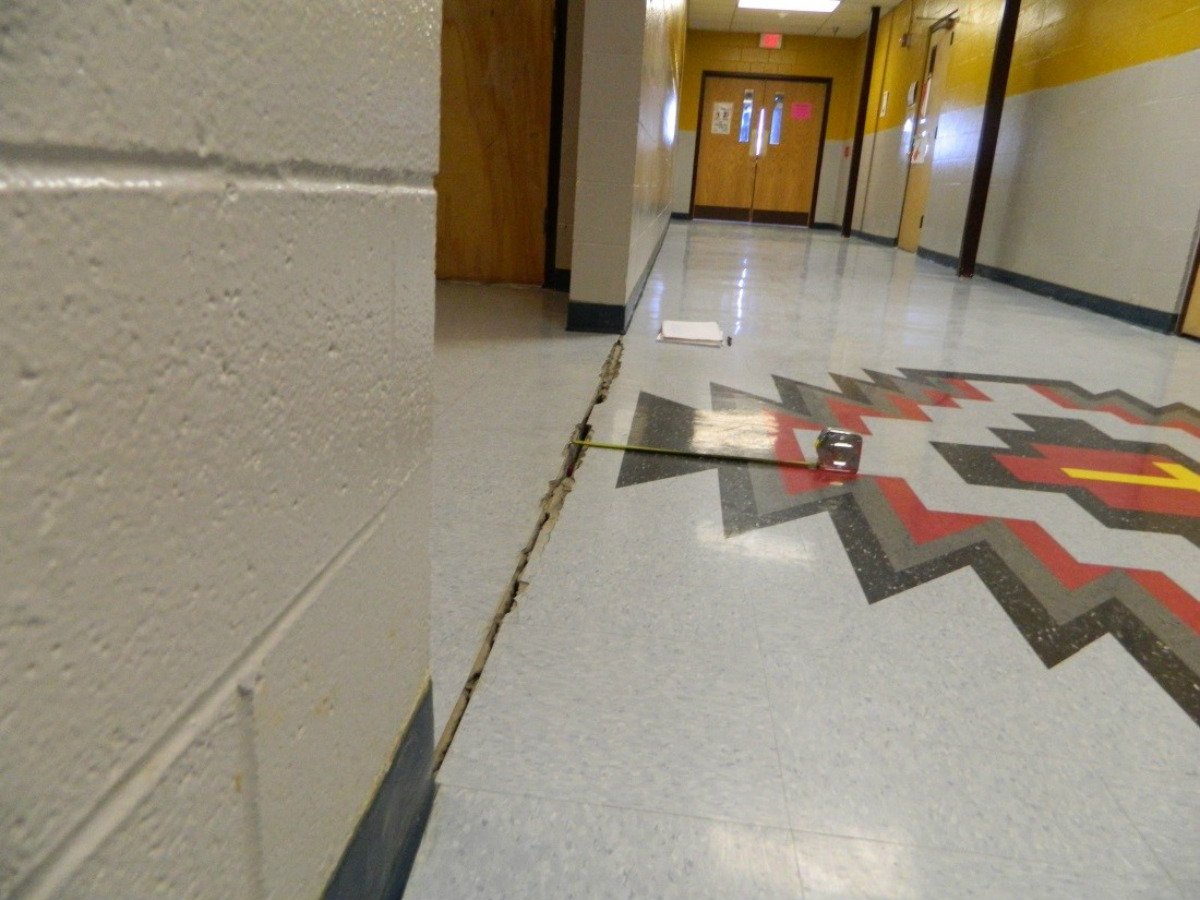 A hallway in a school shows large cracks in its tile floor.
