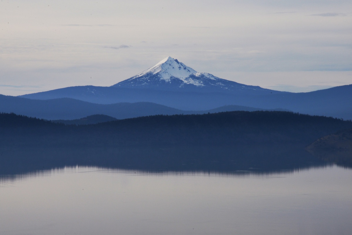 Large white tipped mountain sits behind vegetation and water