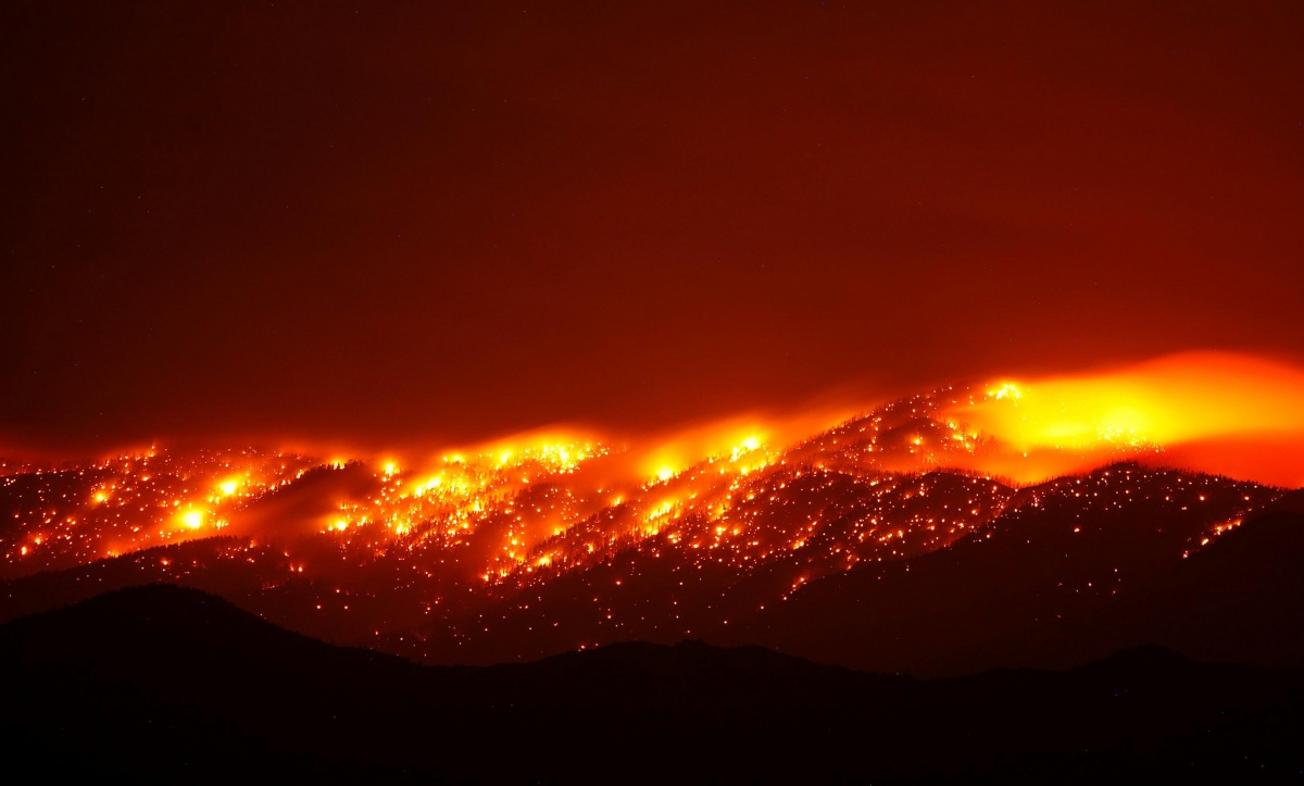 Fire burns brightly in spots along a hillside at night.