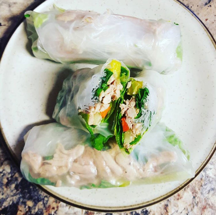 Green vegetables and turkey can be seen through a transparent rice sheet. They are rolled up into four wraps and placed nicely on a white plate.