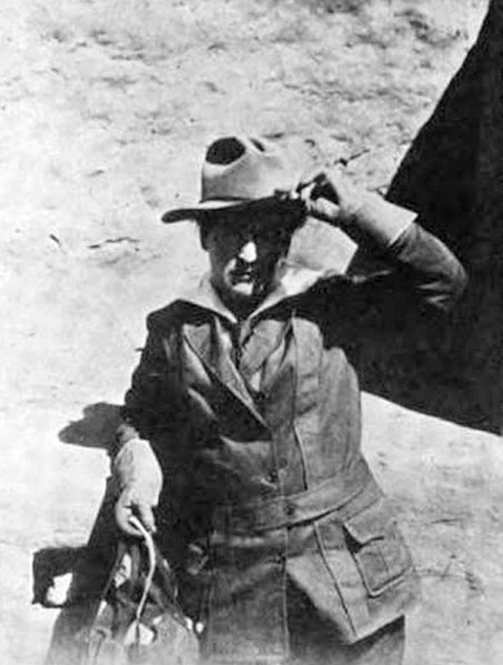An historic black and white photo of Willa Cather in work clothes shielding her eyes from the beaming sun on the old frontier.