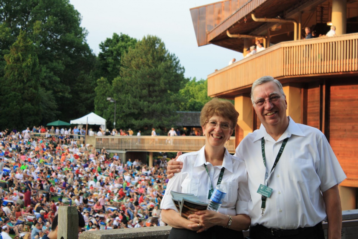 Two volunteers stand with programs in front of a very large crowd.