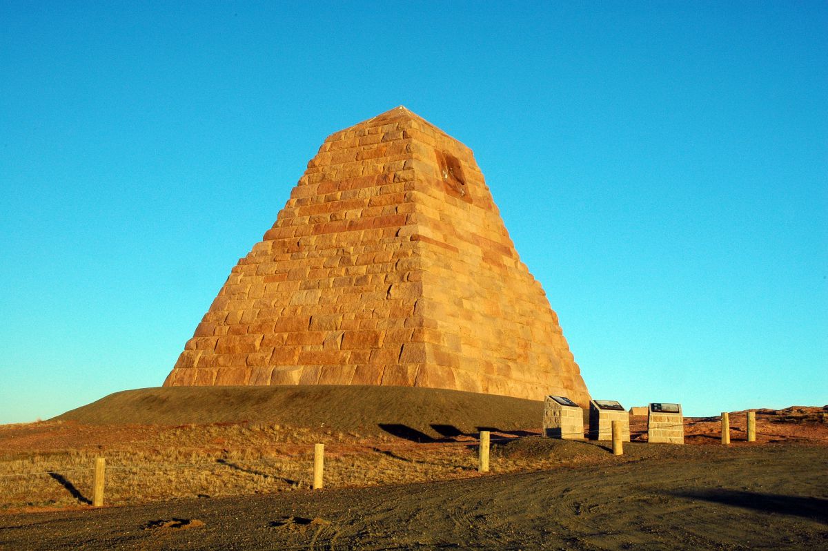 A light brown pyramid-like structure stands in contrast with a vibrant blue sky. 