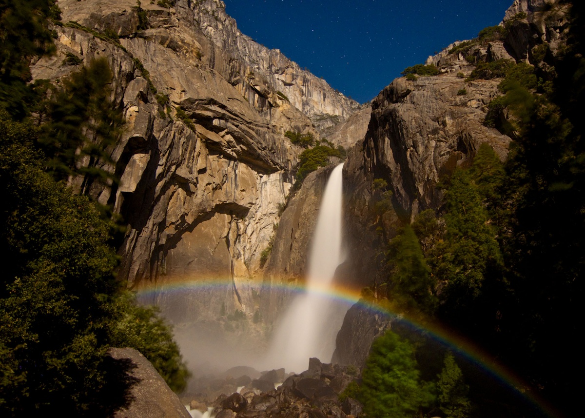 A rainbow in front of a waterfall at night