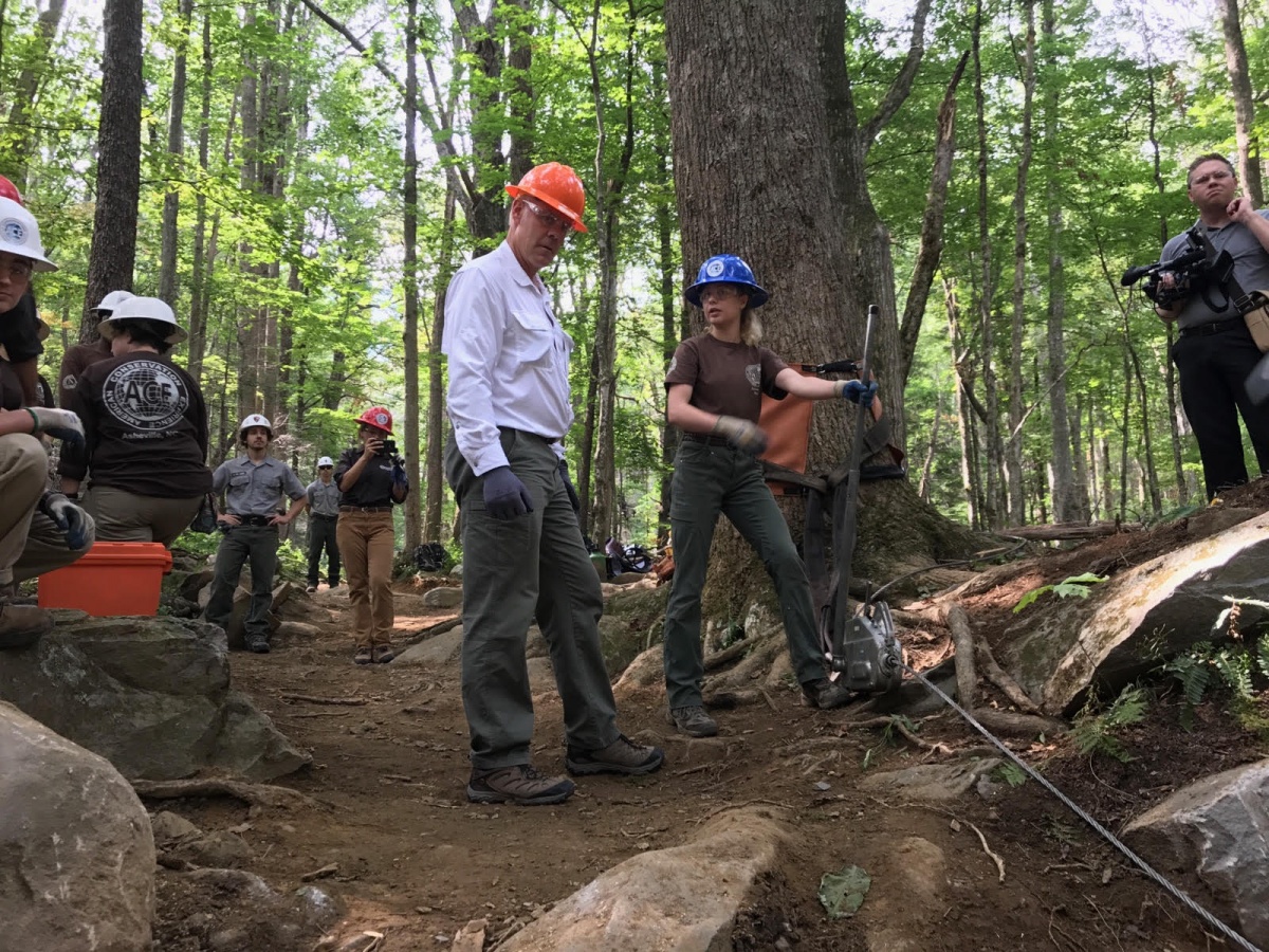 two people wearing hard hats look down at a trail