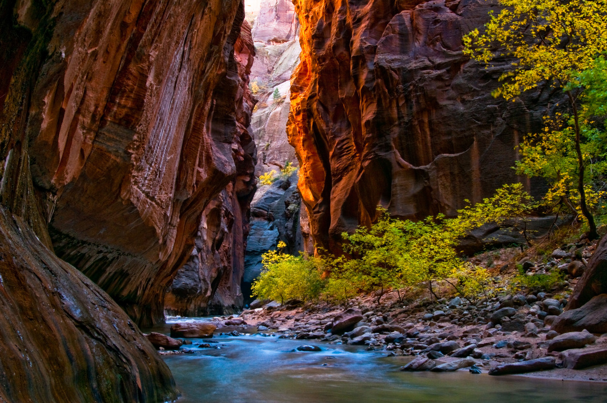 A shallow river flows through a narrow red rock canyon with high walls.