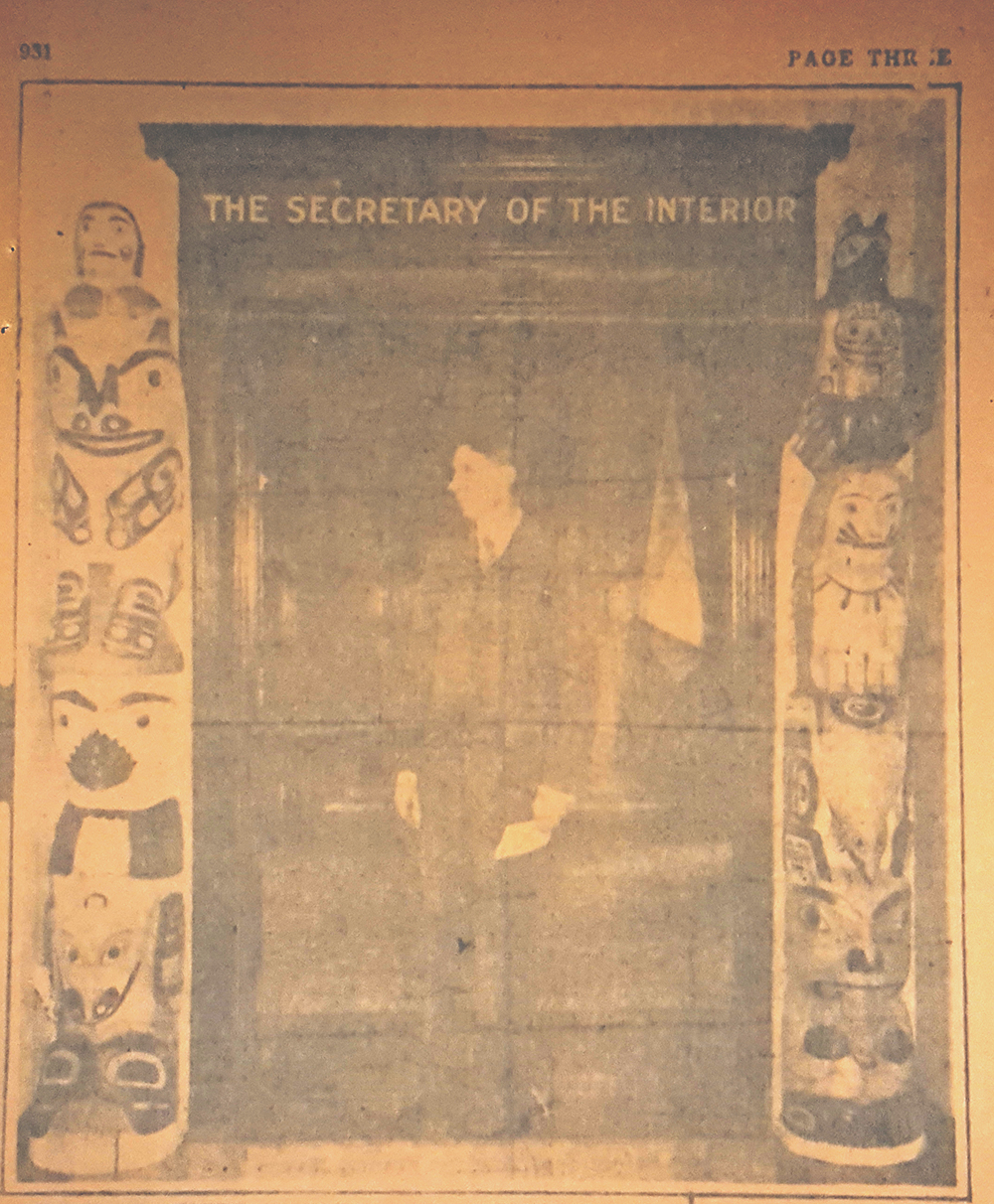 Newspaper clipping with photo of Secretary Wilbur standing between the two totem poles